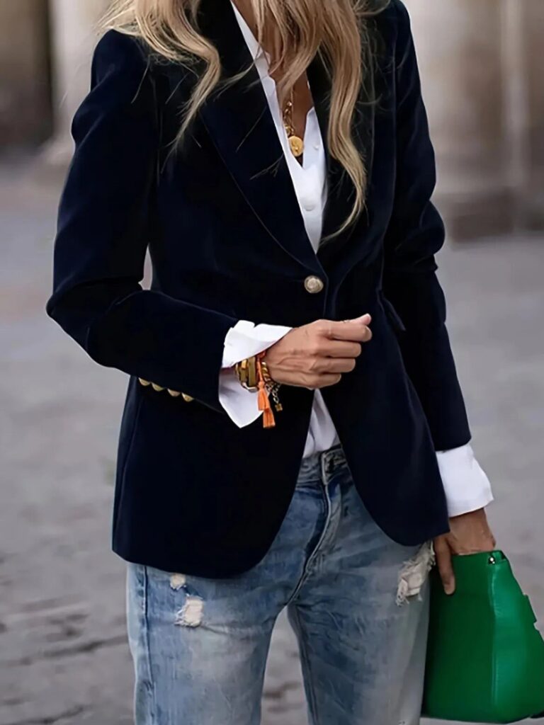 A person wearing a navy velvet blazer, white shirt, and distressed blue jeans.