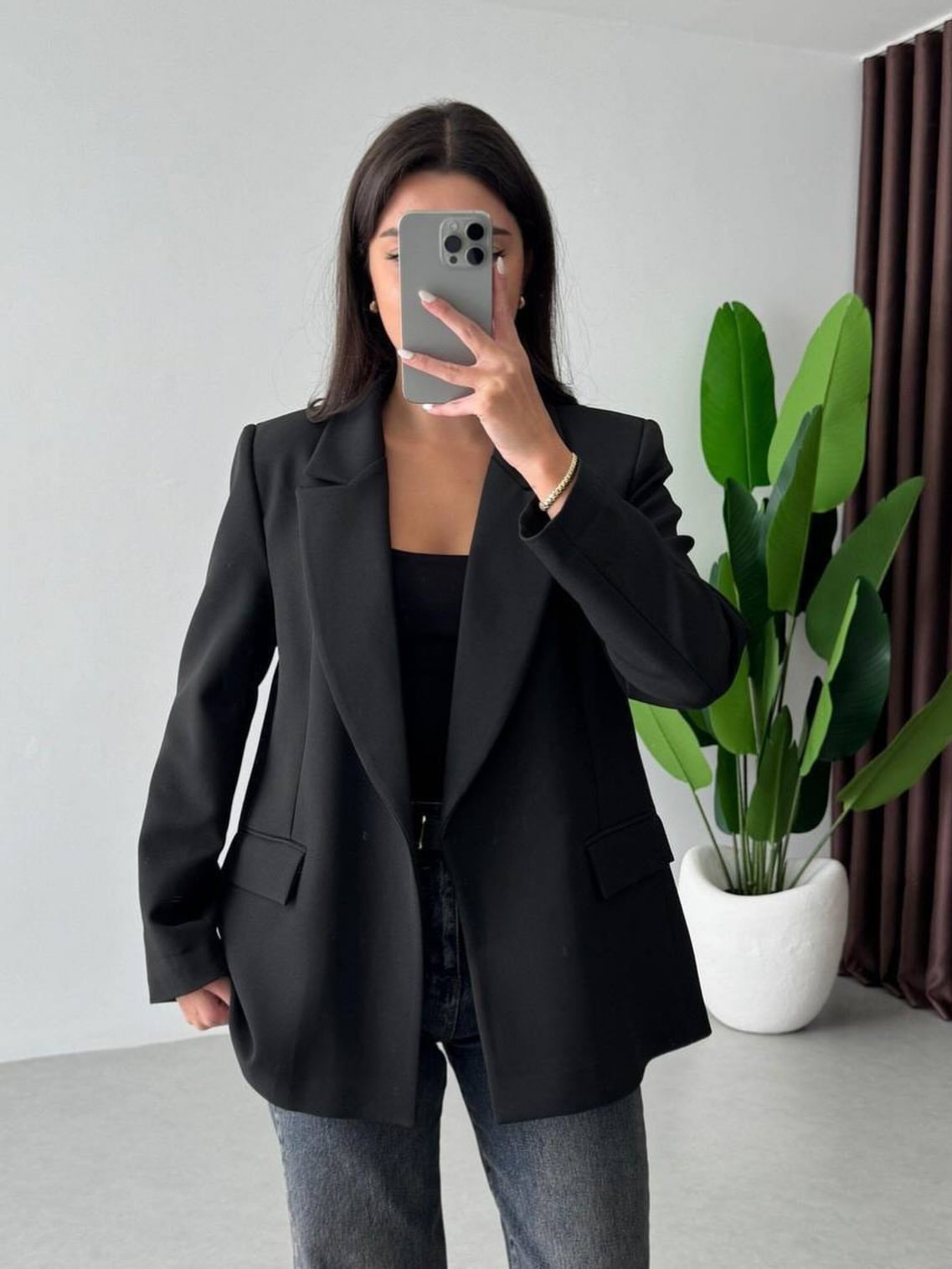 A woman posing in a black blazer, black top, and dark jeans while taking a selfie.