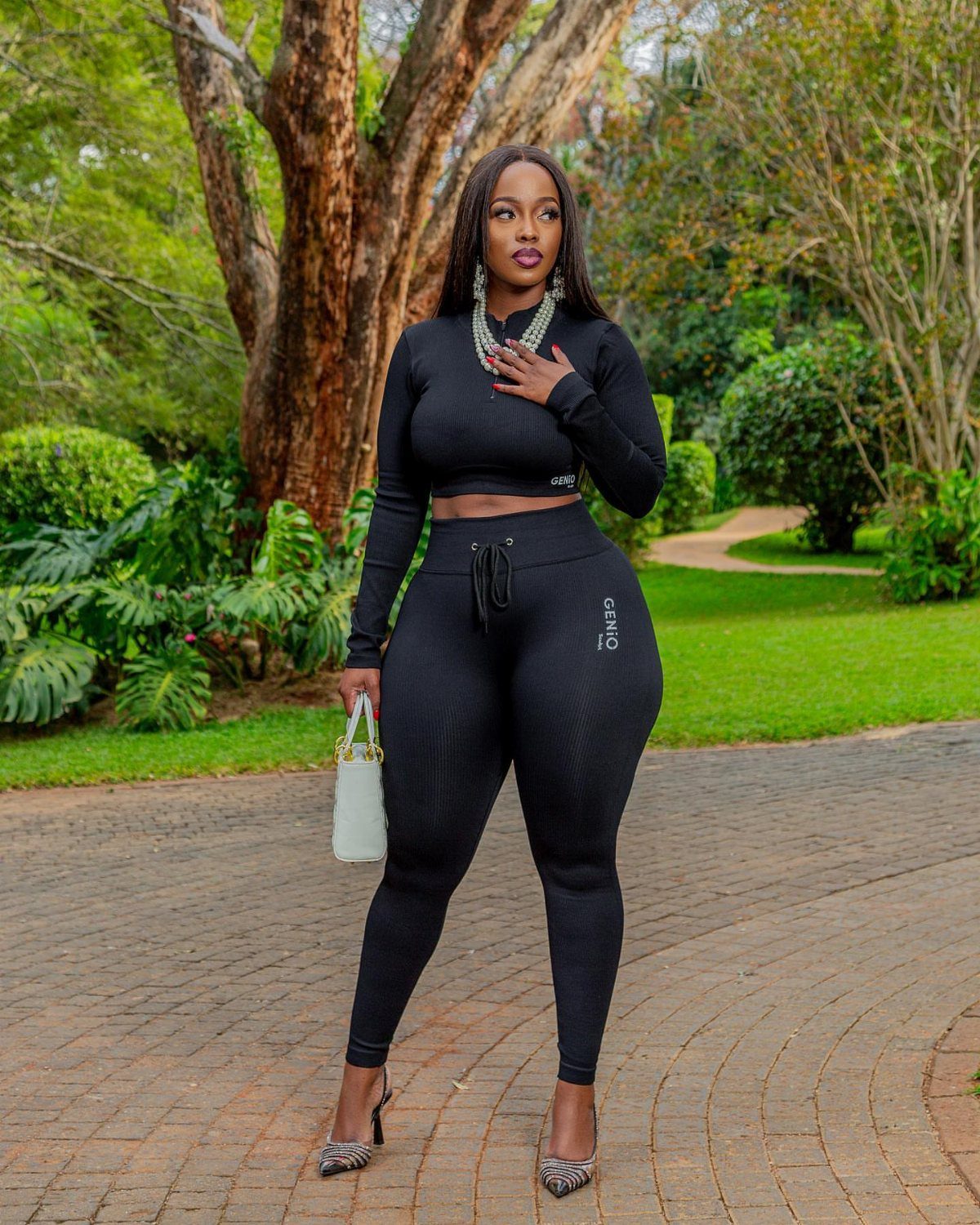 A woman posing in a black long-sleeved crop top and matching black leggings outdoors.