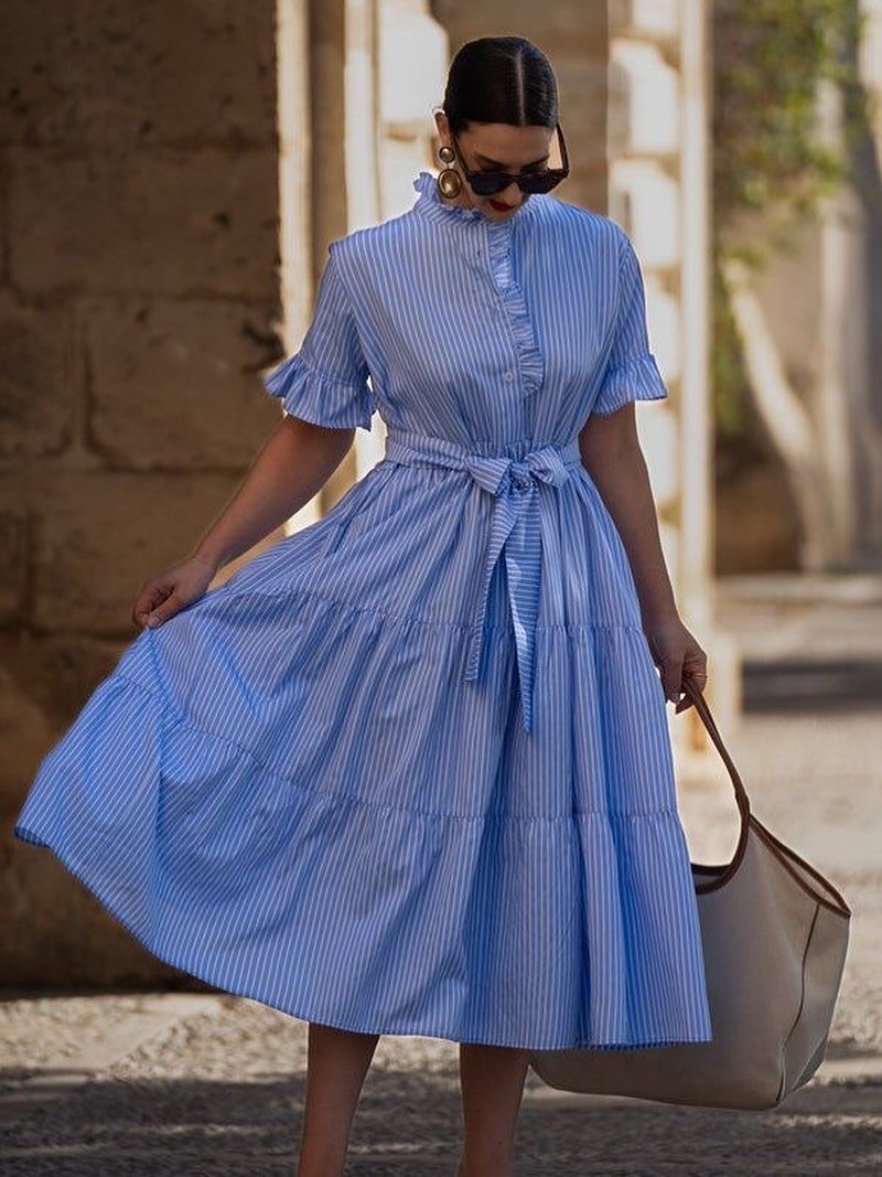 A woman in a blue and white striped midi dress standing outdoors with a large tote bag.