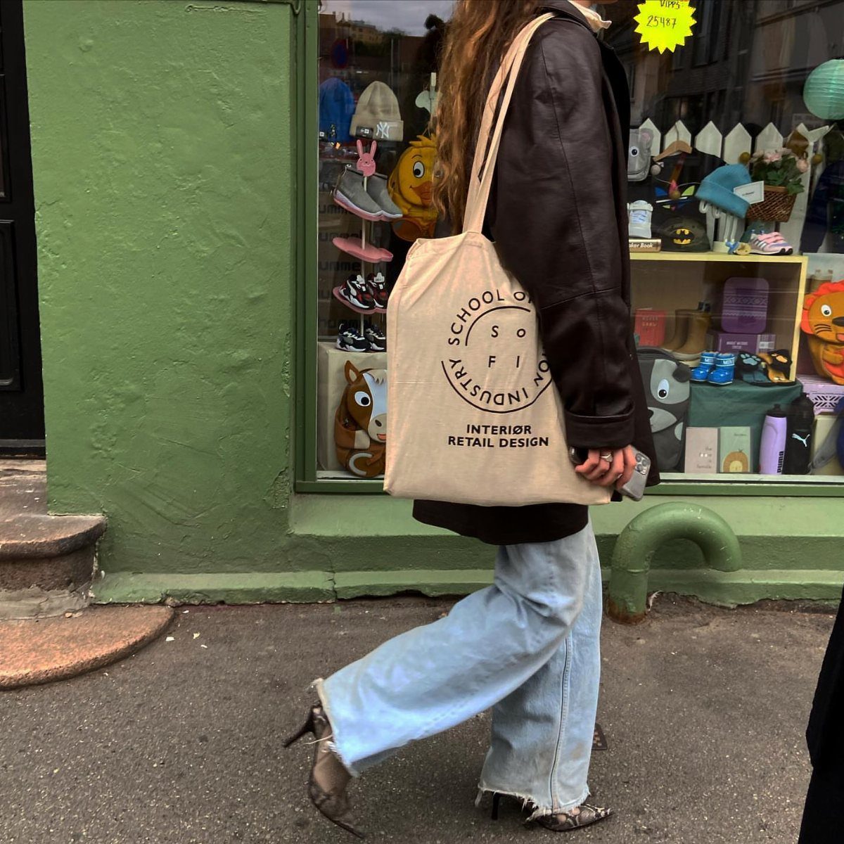 A person walking in a brown leather jacket and light blue jeans carrying a tote bag.