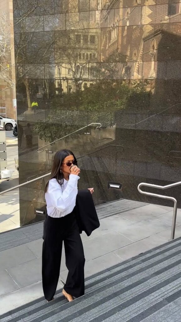 Woman in white blouse and black wide-leg trousers walking down outdoor stairs.