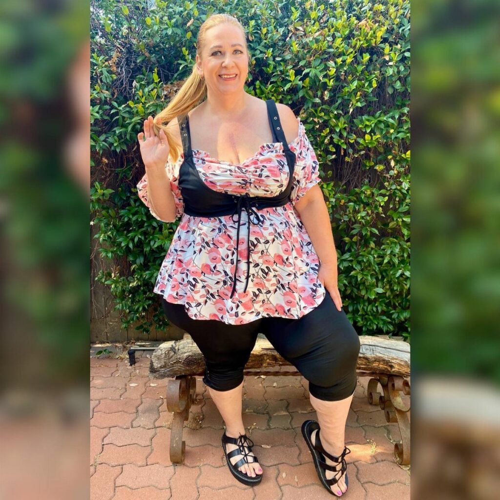 A blonde woman wearing a floral top and black leggings posing outdoors.