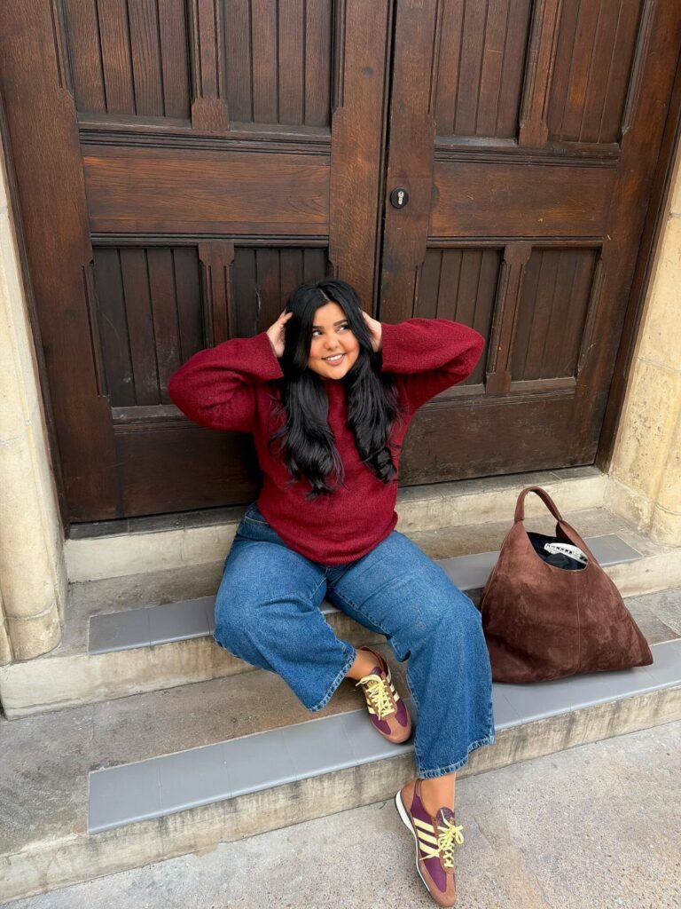 A woman in a maroon sweater and wide-leg jeans sitting on stone steps.