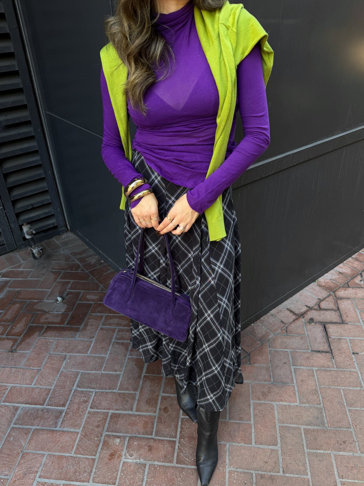 A person wearing a purple turtleneck, plaid skirt, and lime green sweater draped over shoulders.