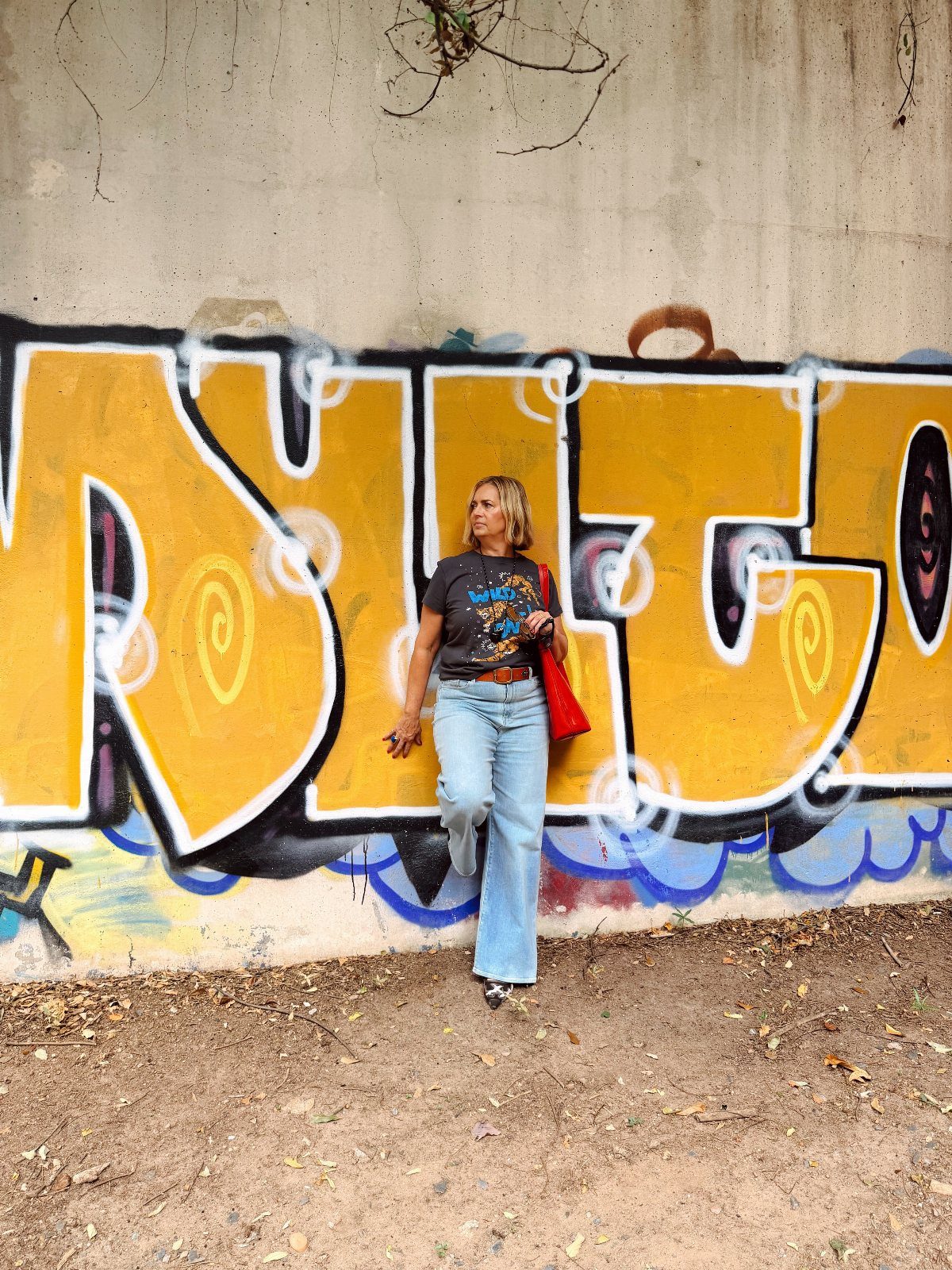 Woman in a graphic t-shirt and light blue wide-leg jeans standing against graffiti.
