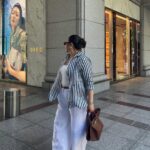 A woman in a striped shirt and white wide-leg trousers walking on a city street.