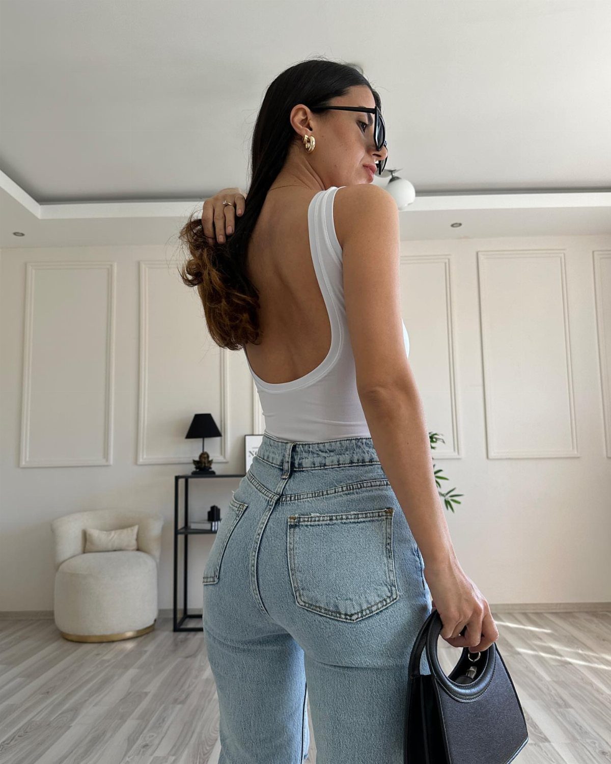 Woman wearing a white sleeveless bodysuit and light blue denim mom jeans while holding a handbag.
