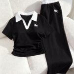 Black polo shirt and matching drawstring pants with white collar and emblem on a white sofa.