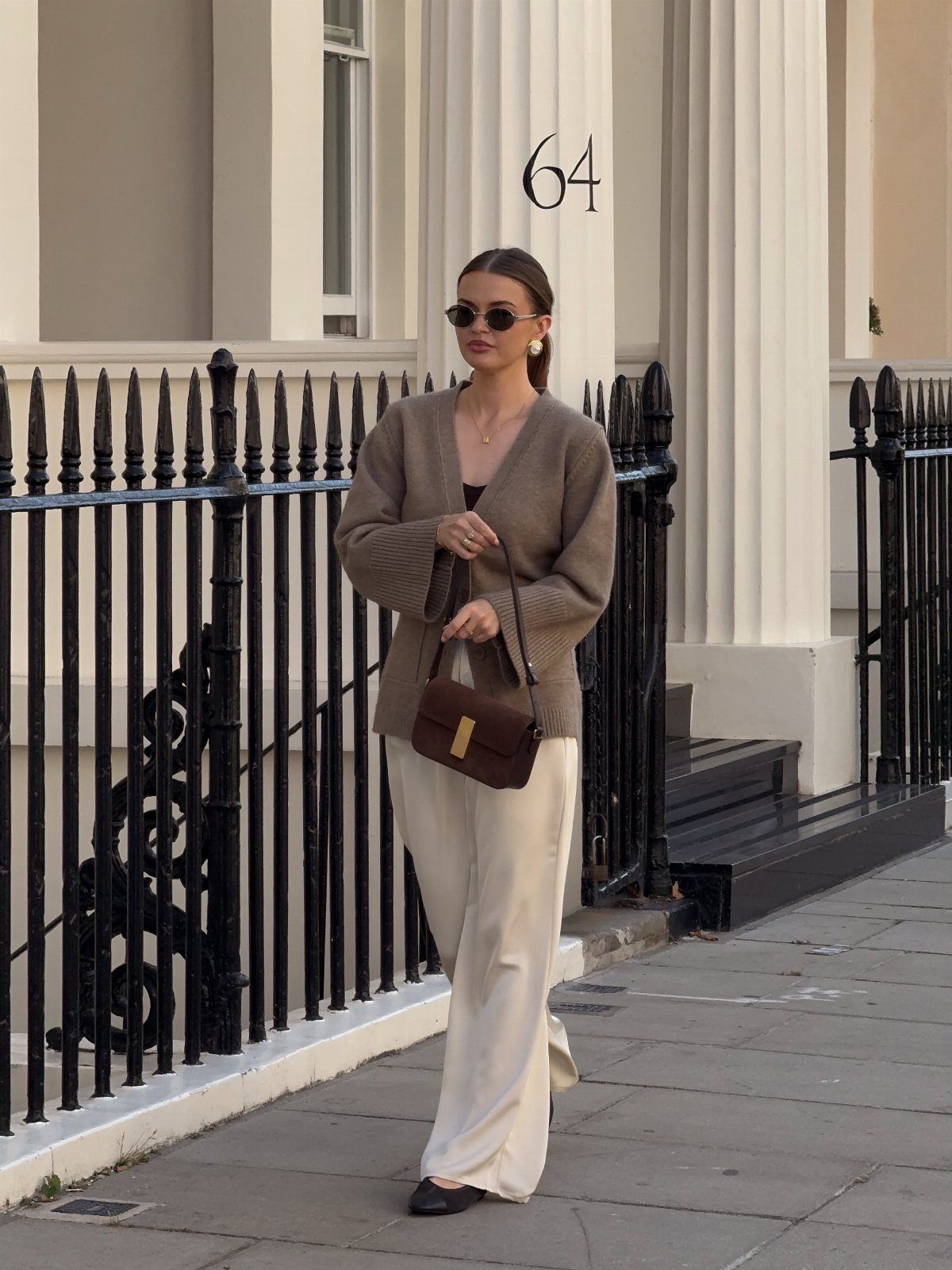 Woman walking in a brown ribbed cardigan, dark top, and cream wide-leg trousers.