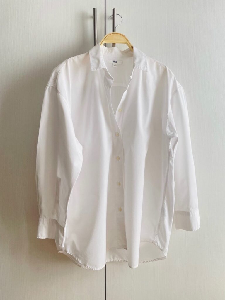 A white long-sleeved button-down shirt hanging on a wooden hanger against a white door.