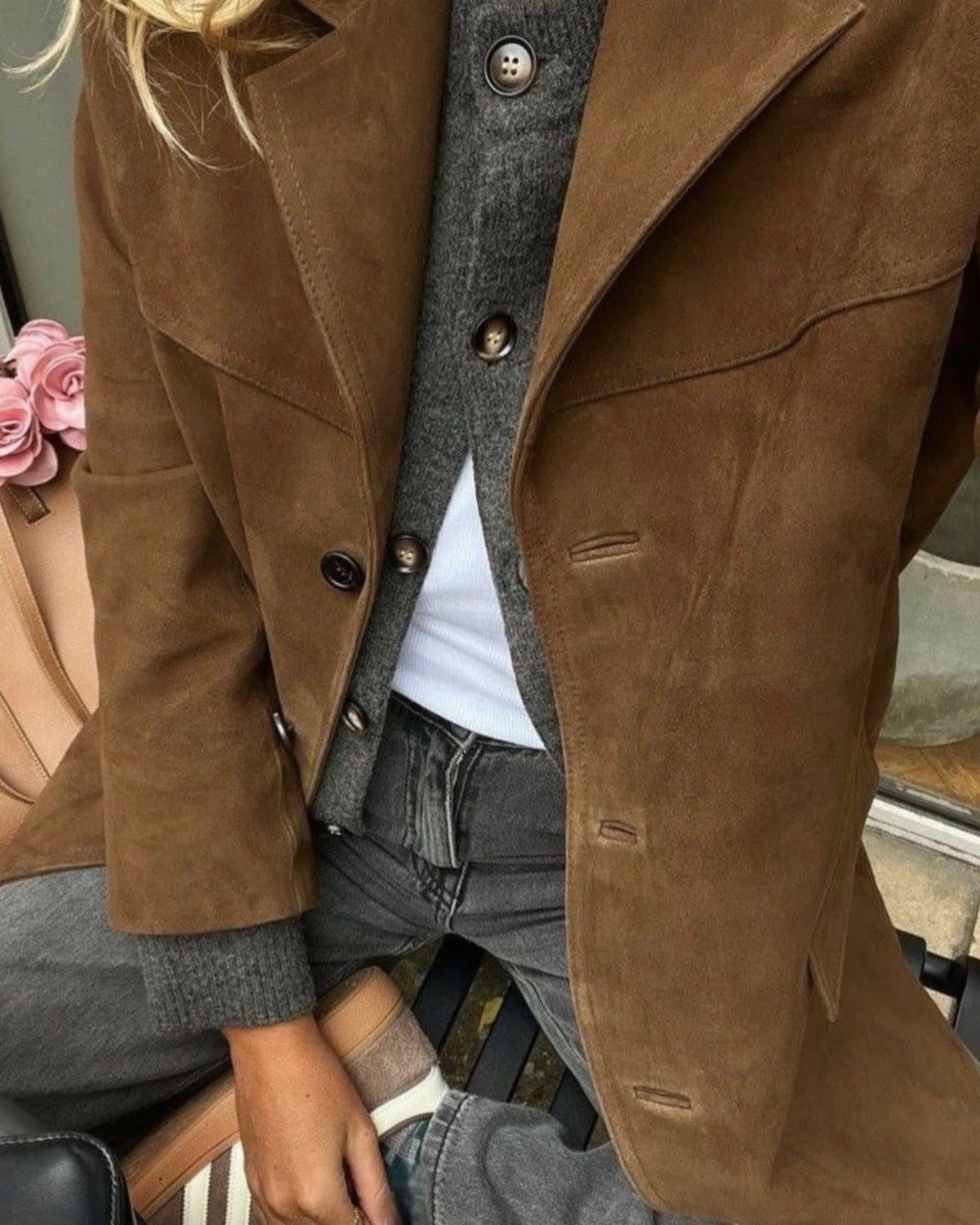 A person wearing a brown suede jacket over a grey cardigan and white shirt.