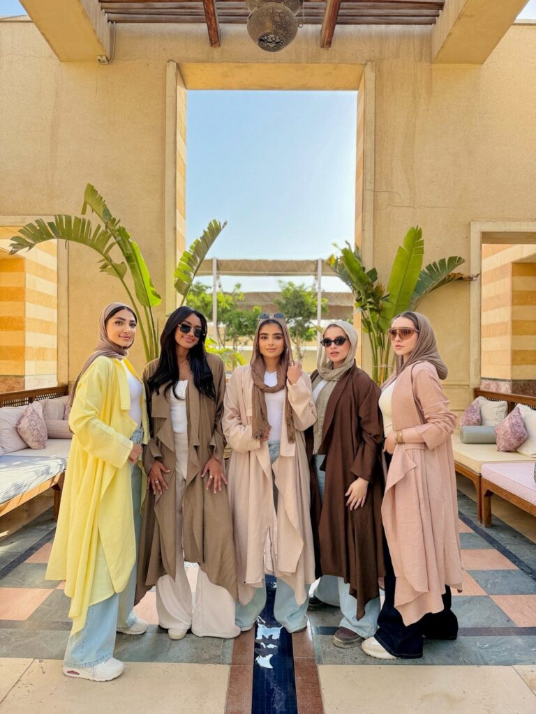 Five women posing in a courtyard wearing various long, flowing waterfall style jackets in warm autumn tones.