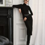 Woman wearing a black turtleneck and matching midi skirt with silver chain detail and black boots.