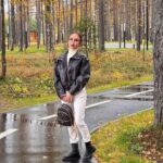 Woman wearing white jeans and a black leather jacket standing on a wet forest path.